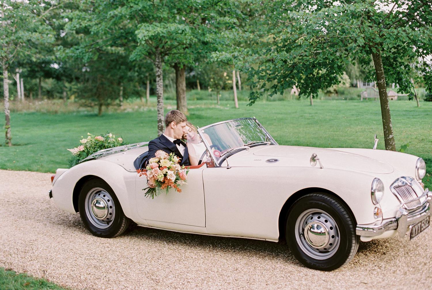 married couple sitting in classic vintage wedding car decorated with peach colour flowers and greenery