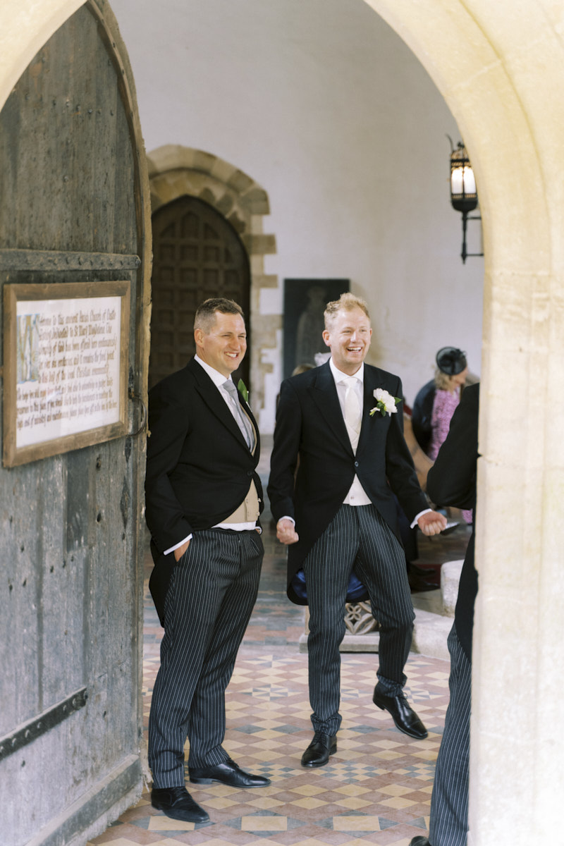 groom and groomsmen waiting for wedding guests arriving at the st mary magdalene church in castle ashby