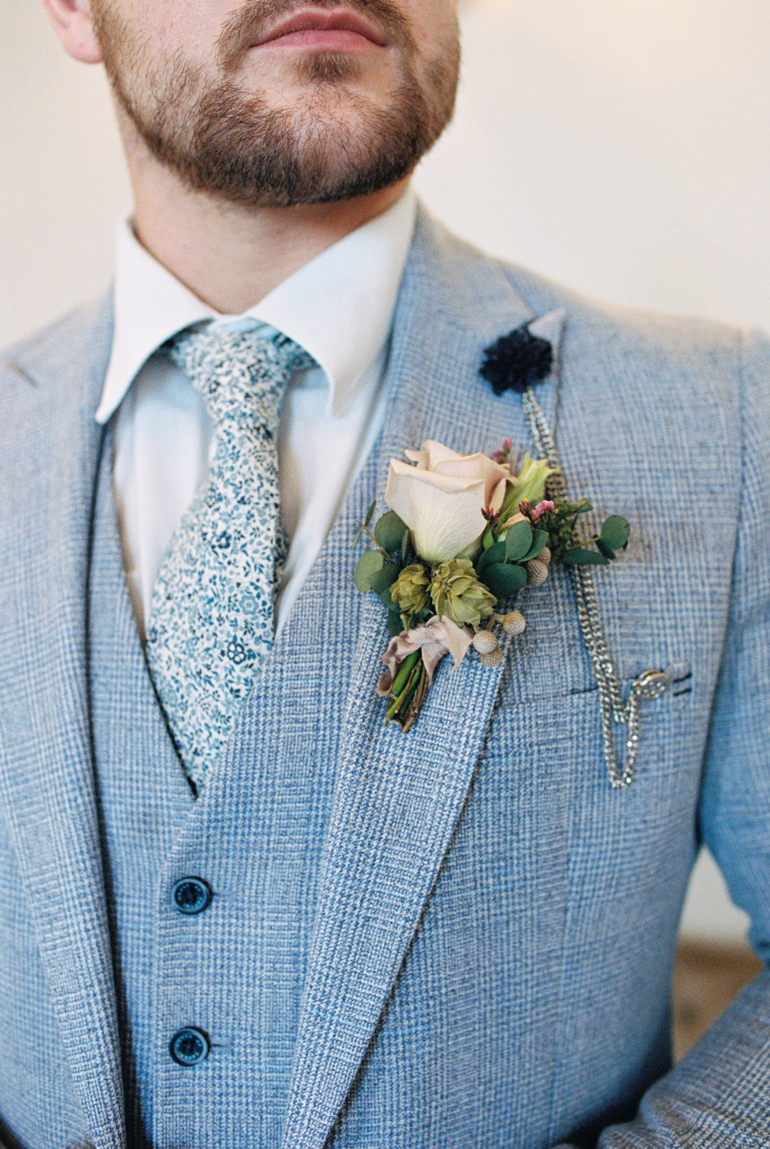 close up groom's boutonniere with single rose and greenery wrapped with silk ribbon
