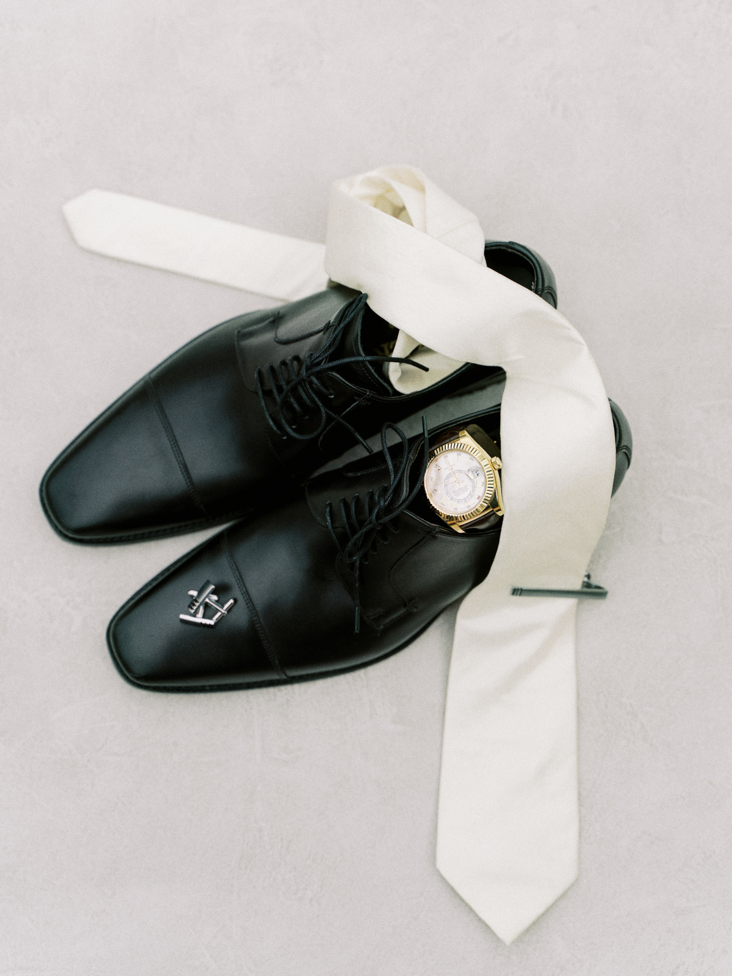 black groom's shoes with white tie, cufflinks and watch capture on a styling board