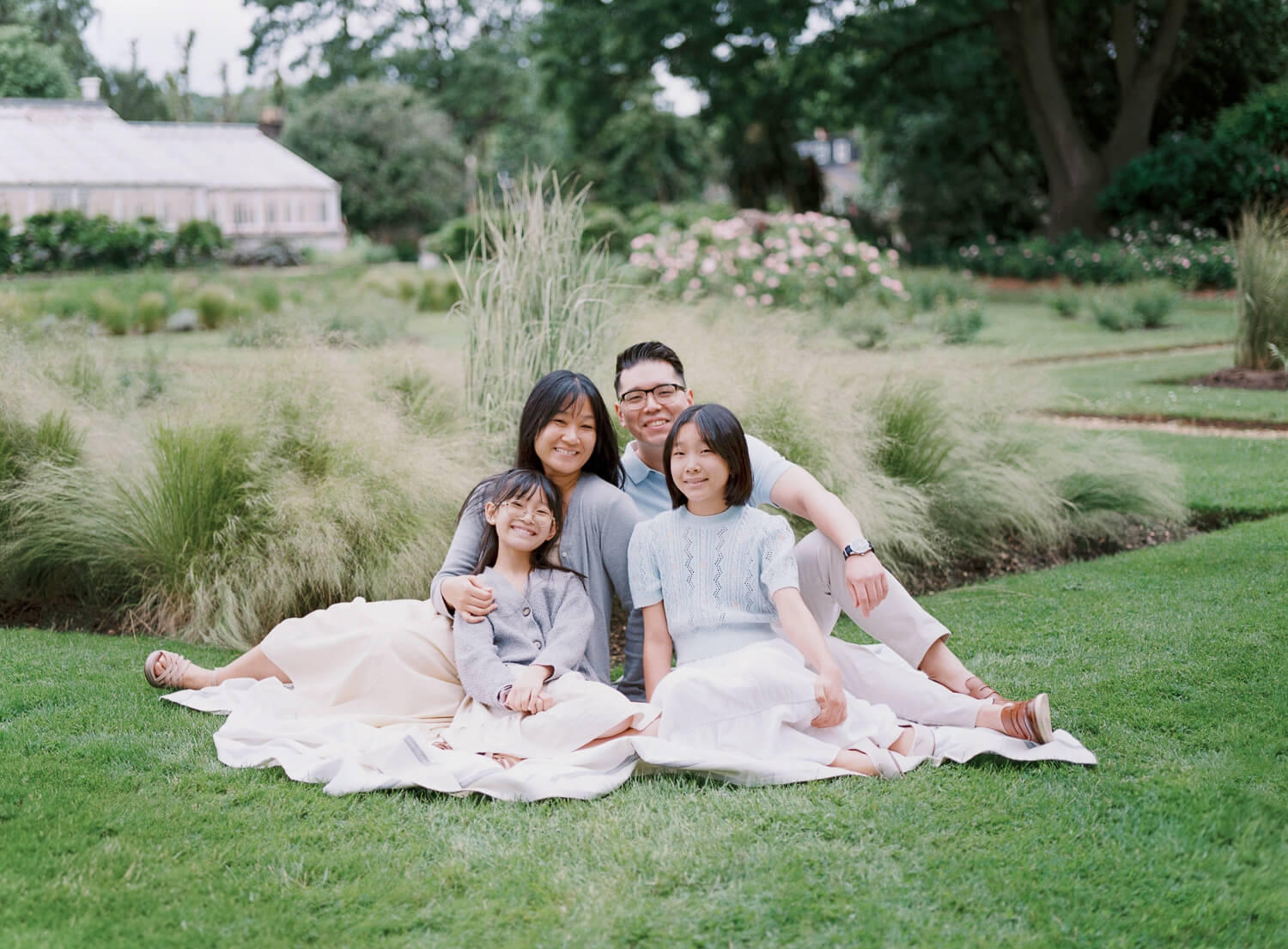 parents and two daughters sitting on the blanket in the garden and smiling at their family photo session at chiswick gardens and house