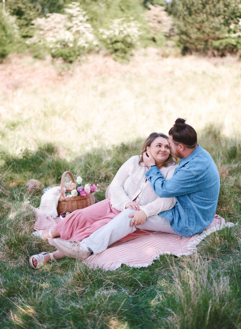 couple sitting on the pink picnic blanket at park and looking at each other and sharing smiles