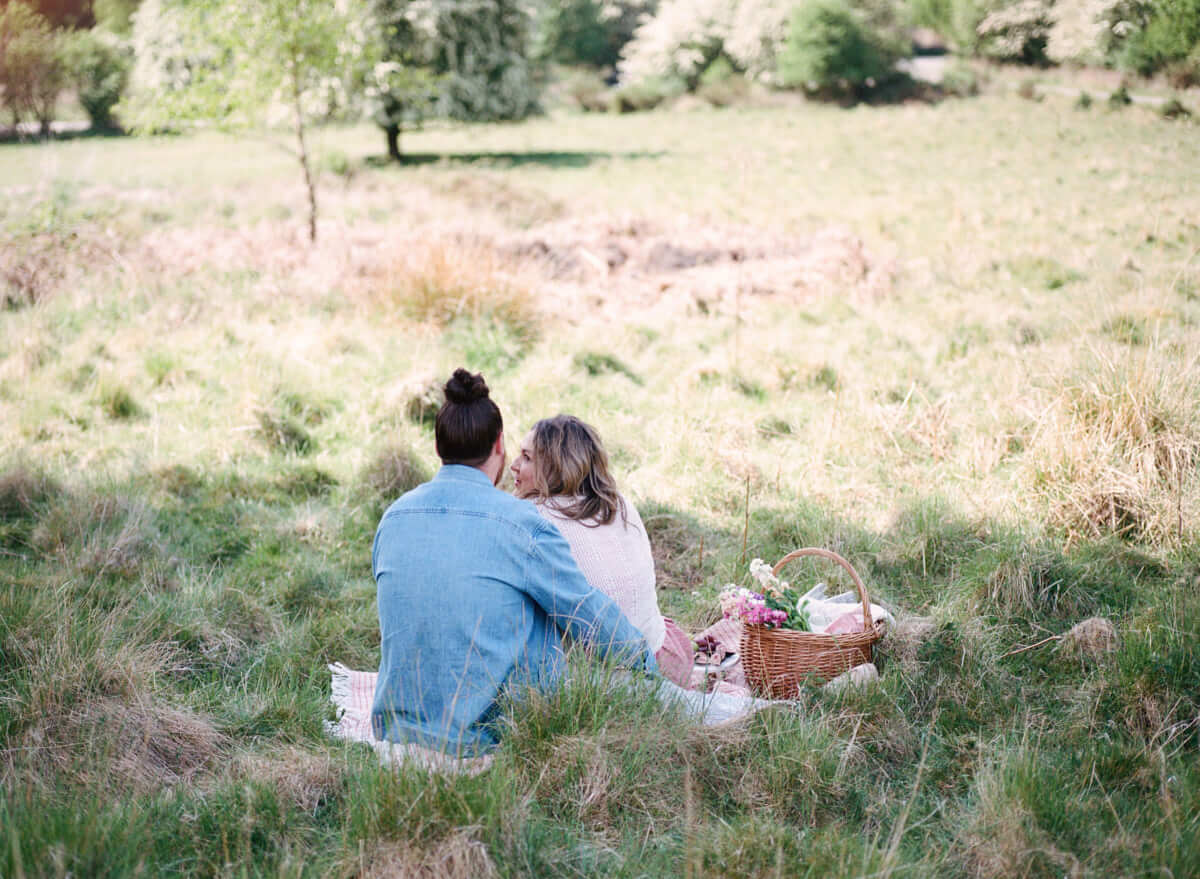 couple sitting on the picnic blanket and looking at each other in the park