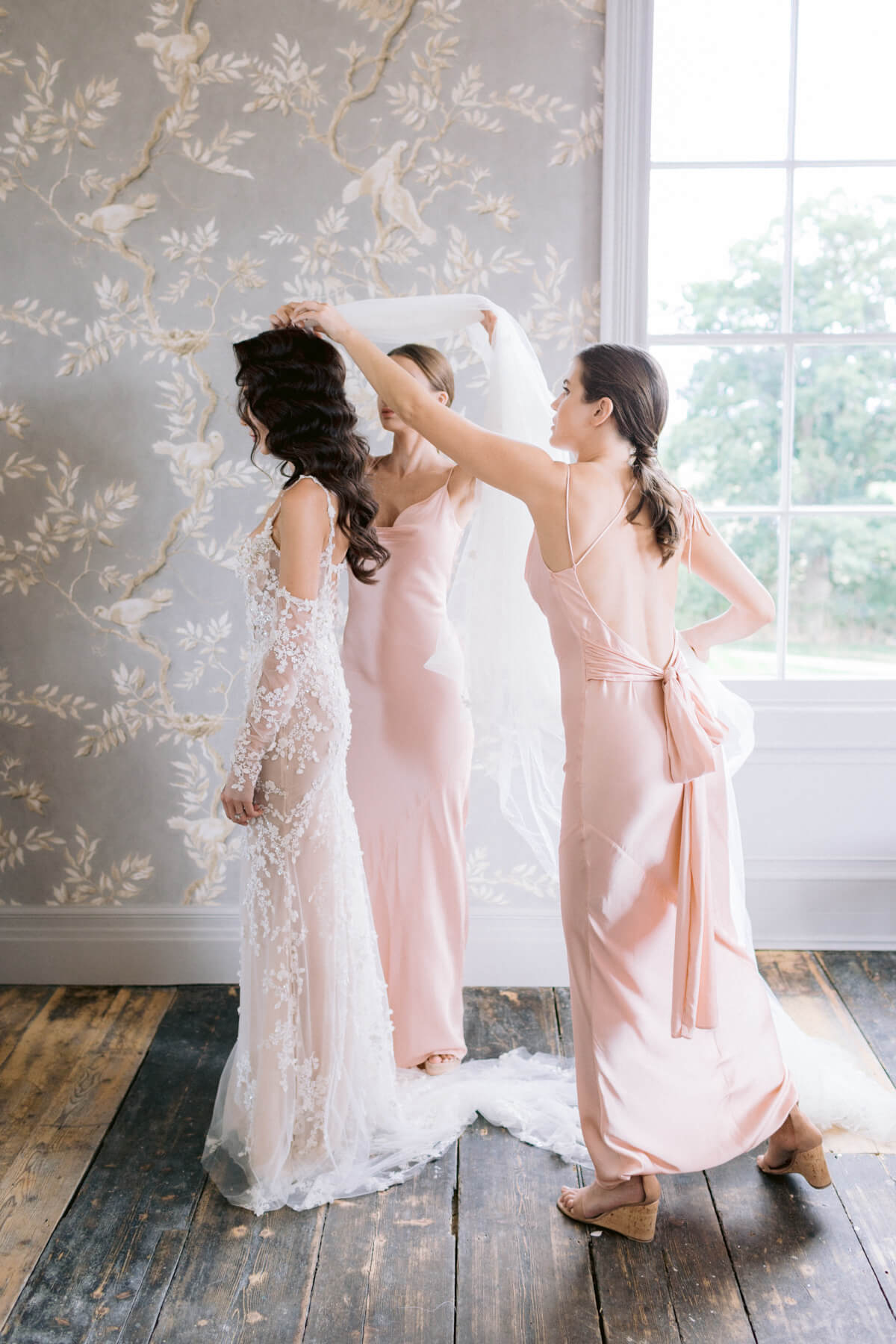 Bright and airy wedding photography style showing a beautiful natural moment of the bride getting ready while the bridesmaids are putting the veil on 
